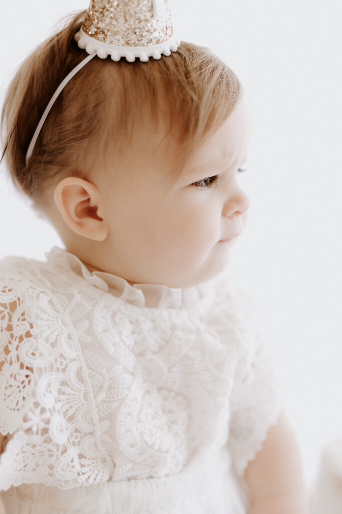 Profile portrait of One-year-old baby girl in a lace dress and a glittery party hat at her milestone portrait session in Roseville, CA. 