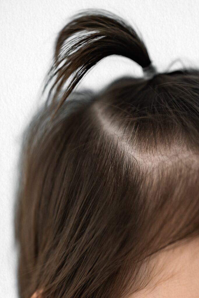 Close-up of a child's head with brown hair tied in a small ponytail on top, against a white background—perfect for milestone photography by your Sacramento family photographer.