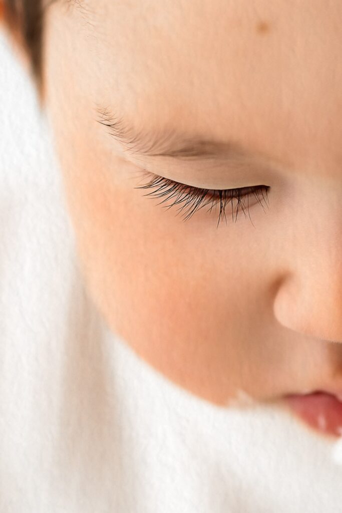 Close-up of a baby's face with closed eye, long eyelashes, and soft skin against a white background, captured by a Roseville CA photographer specializing in in-home studio photography.